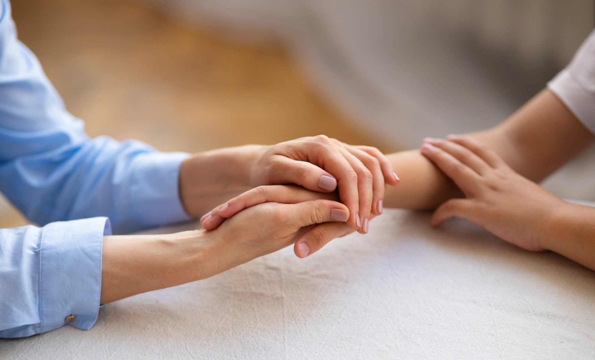 Ein Mensch in einem blauen Hemd hält die Hand einer anderen Person in seinen beiden Händen.