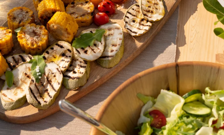 Gegrilltes Gemüse (Mais, Tomate und Zucchini) und ein grüner Salat auf einem gedeckten Tisch.